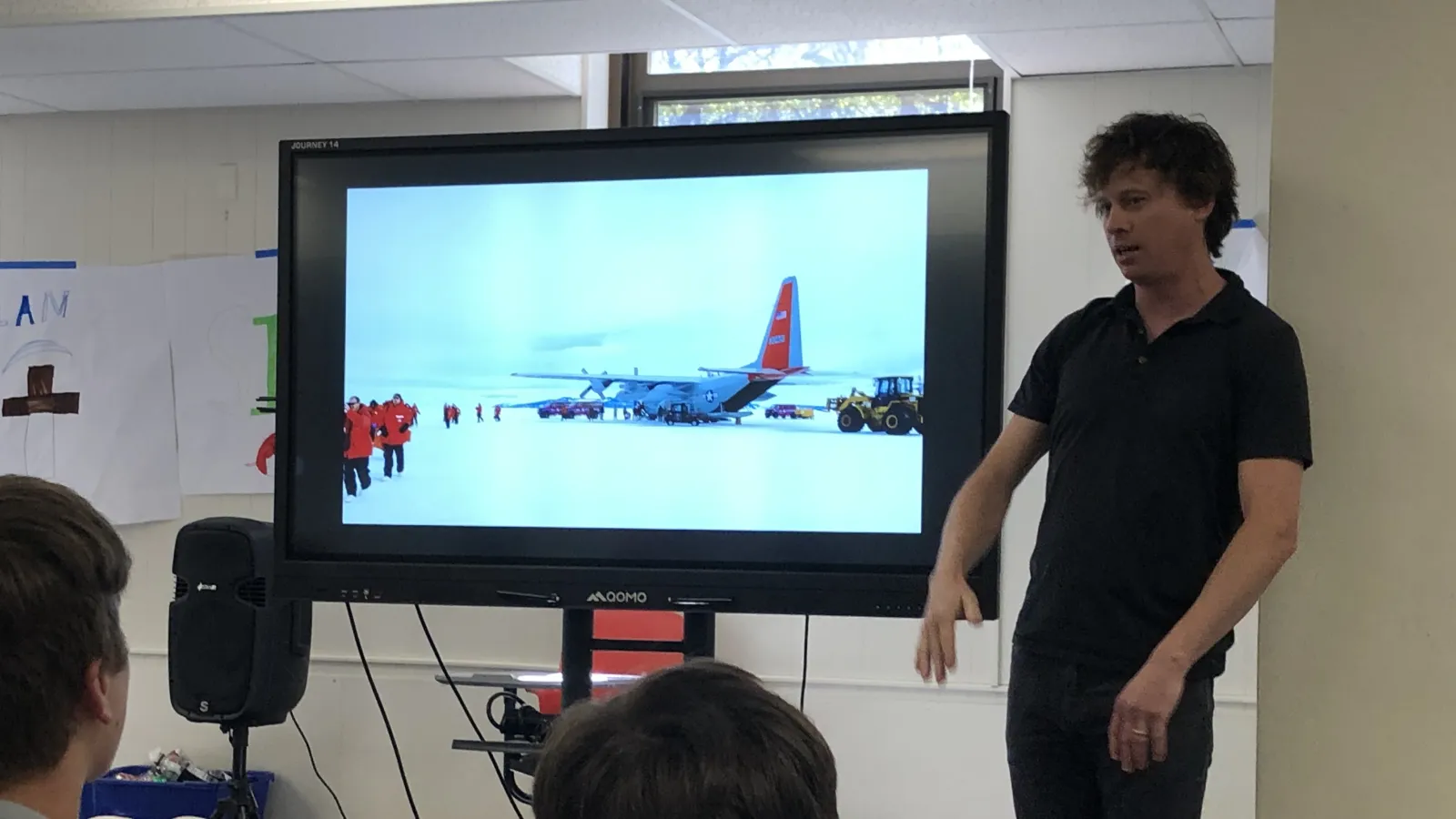 researcher presenting to students with a video display showing Antarctica.