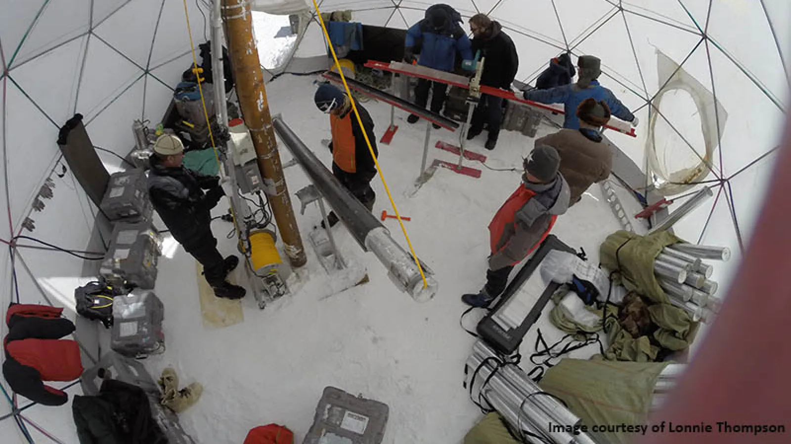 Above view inside a dome with equipment and people standing around on the snow covered ground.