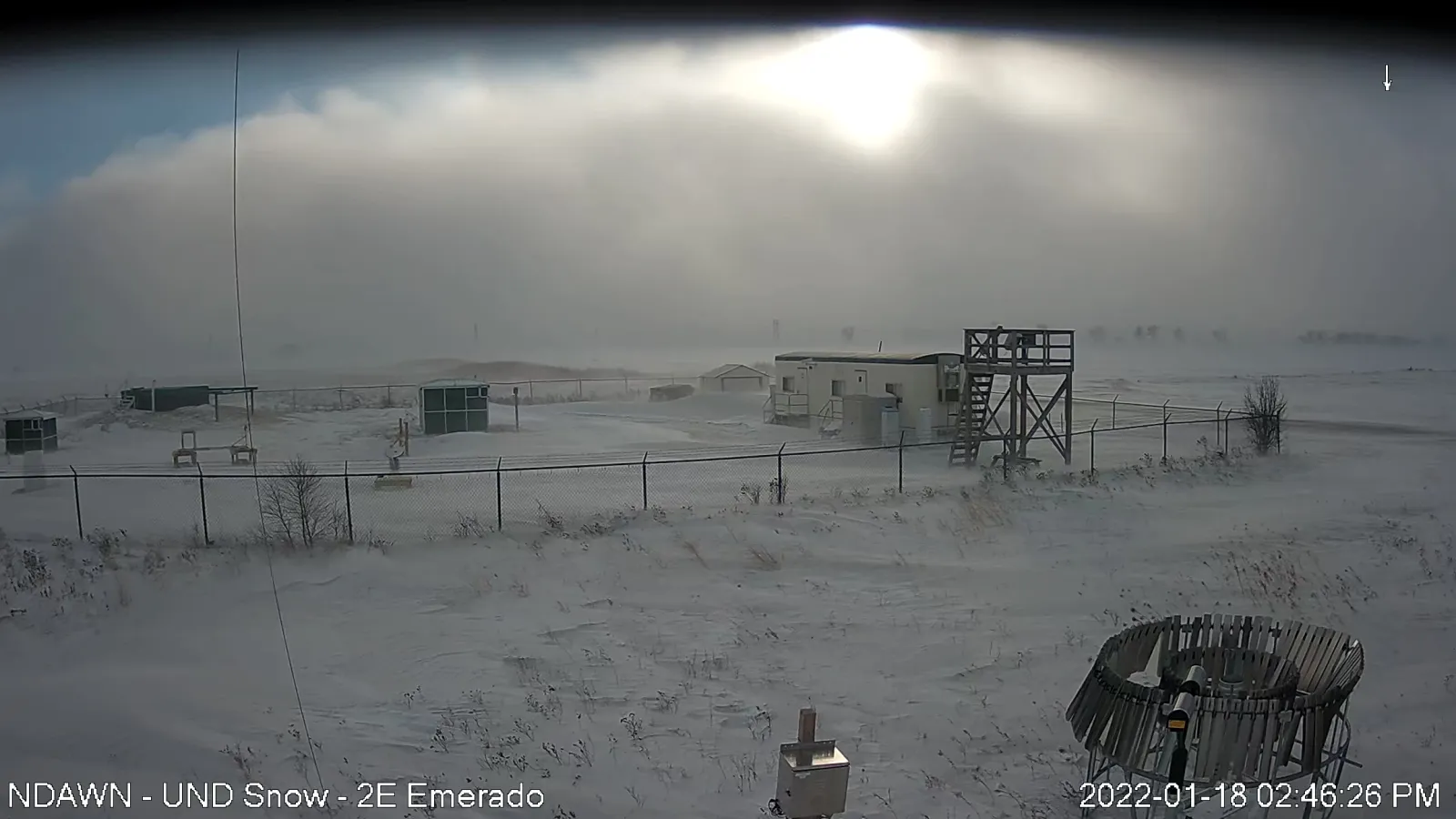 A snow covered landscape with buildings and structures and sunlight behind the white clouds