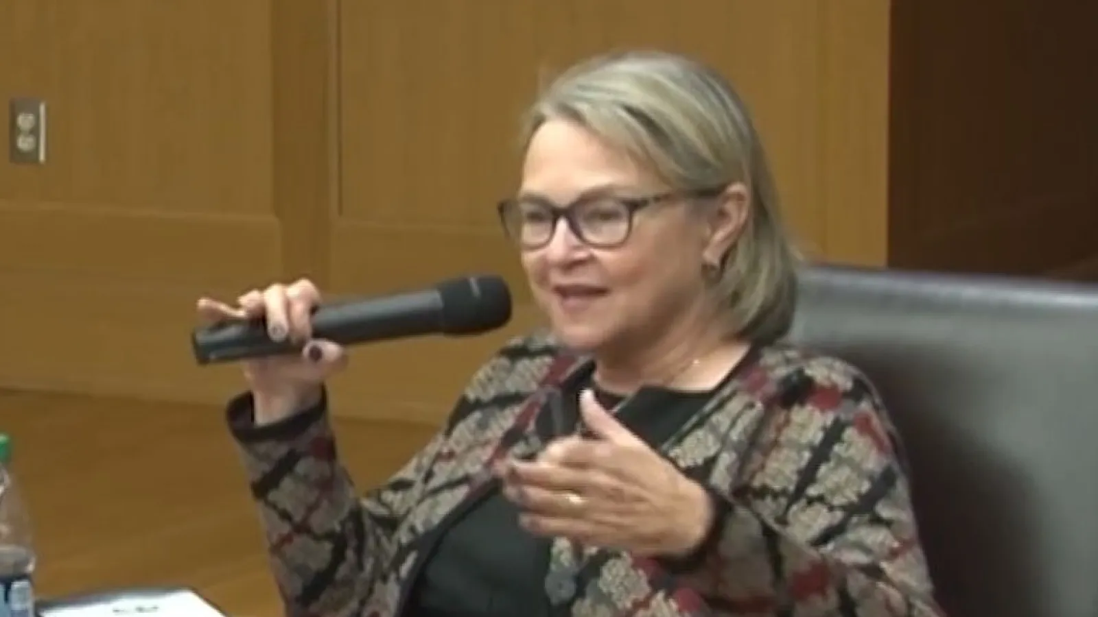 Ann Fisher sitting on a couch speaking in a hand held microphone