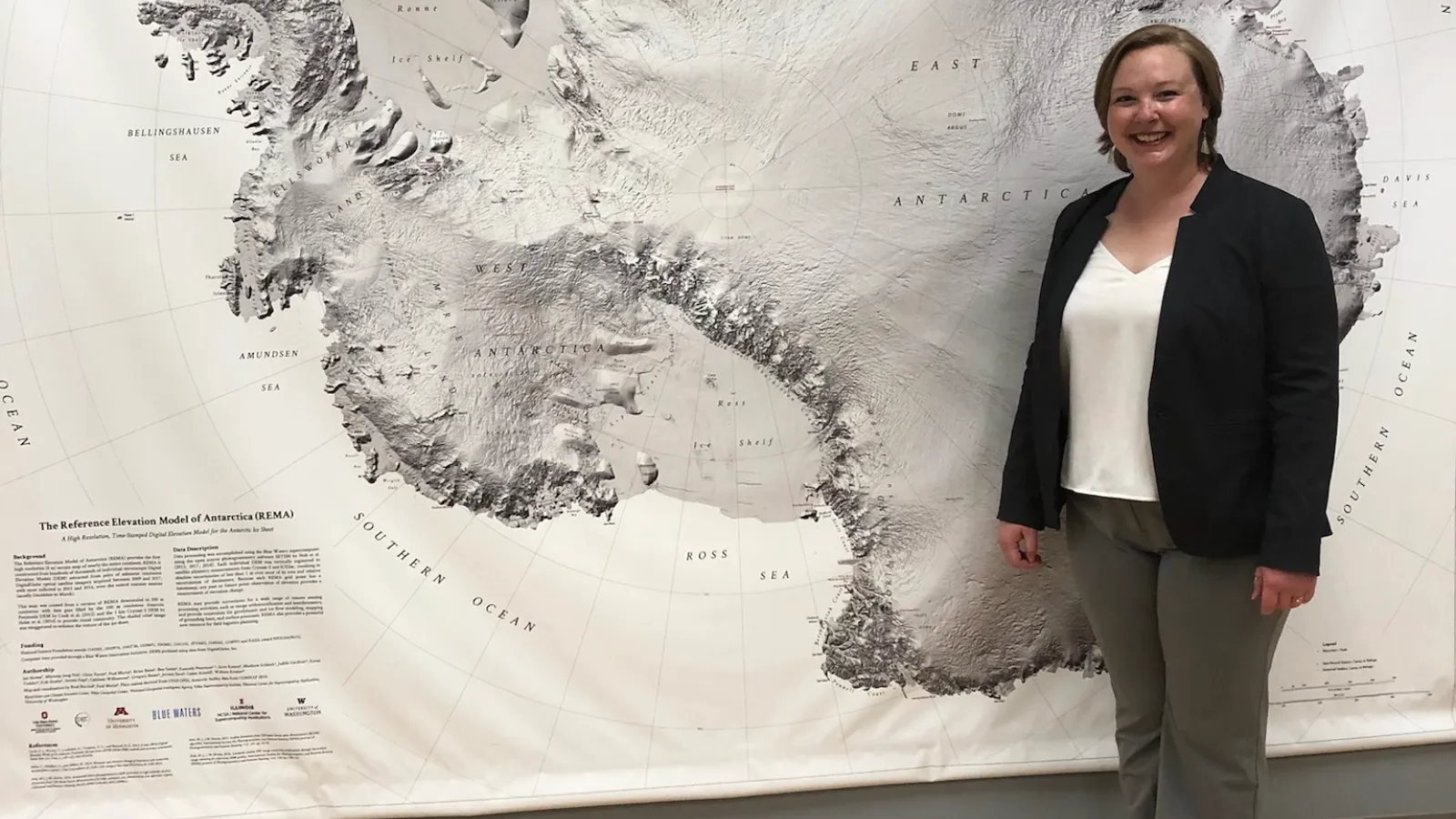 A white woman with short, blonde hair standing in front of a map of Antarctica