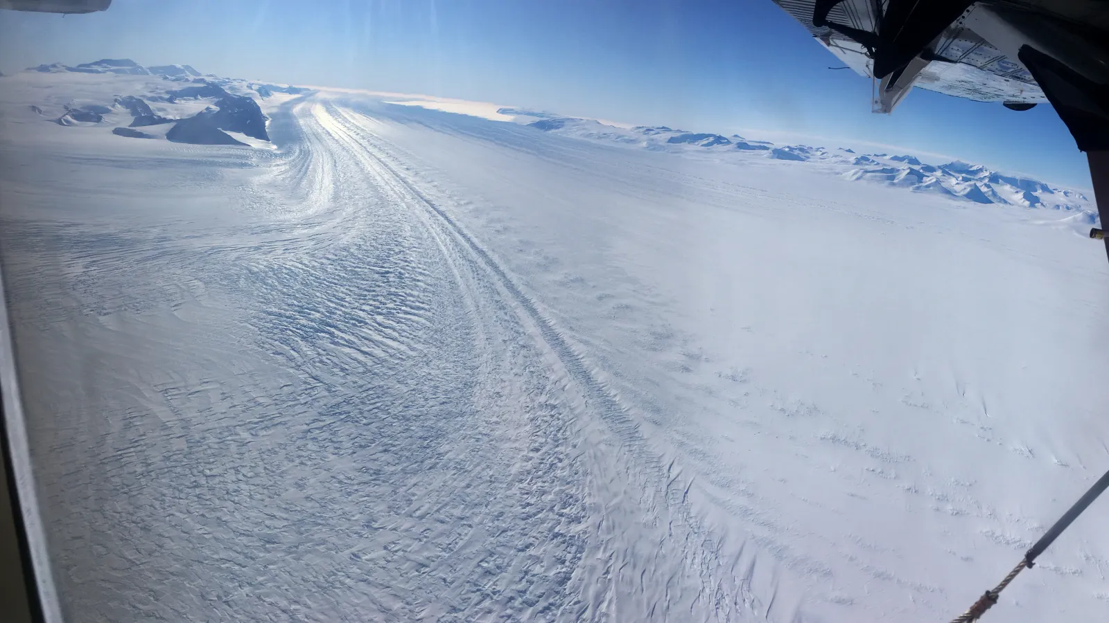 Snow covered ground from a plane with part of the plane in view