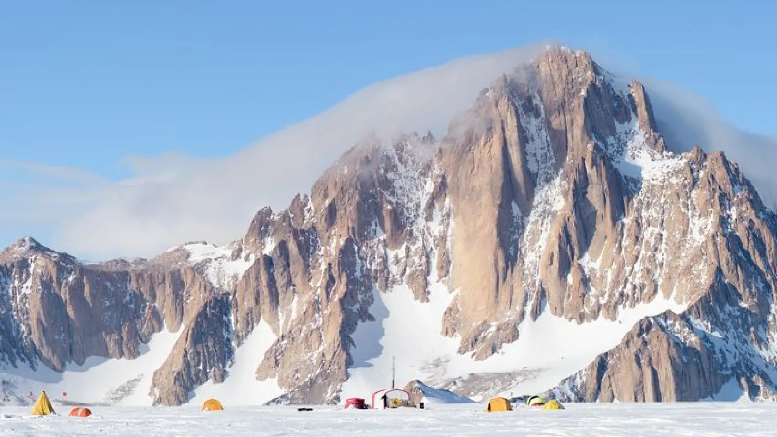 Rocky mountain with some white clouds and blue skies in the background and tents pitched in the foreground.