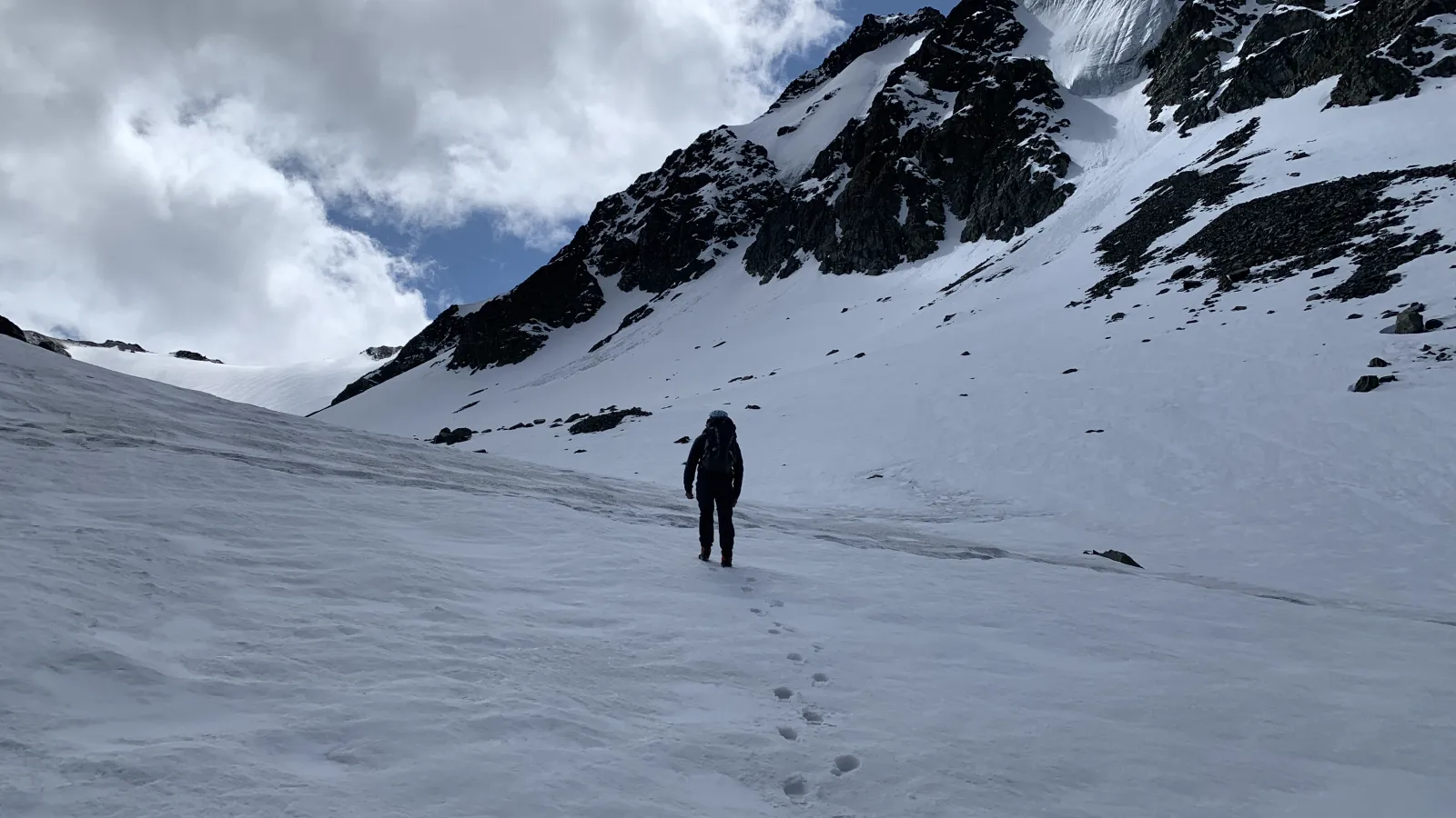 someone walking in a snow covered mountainous region. Blue skies and white clouds.