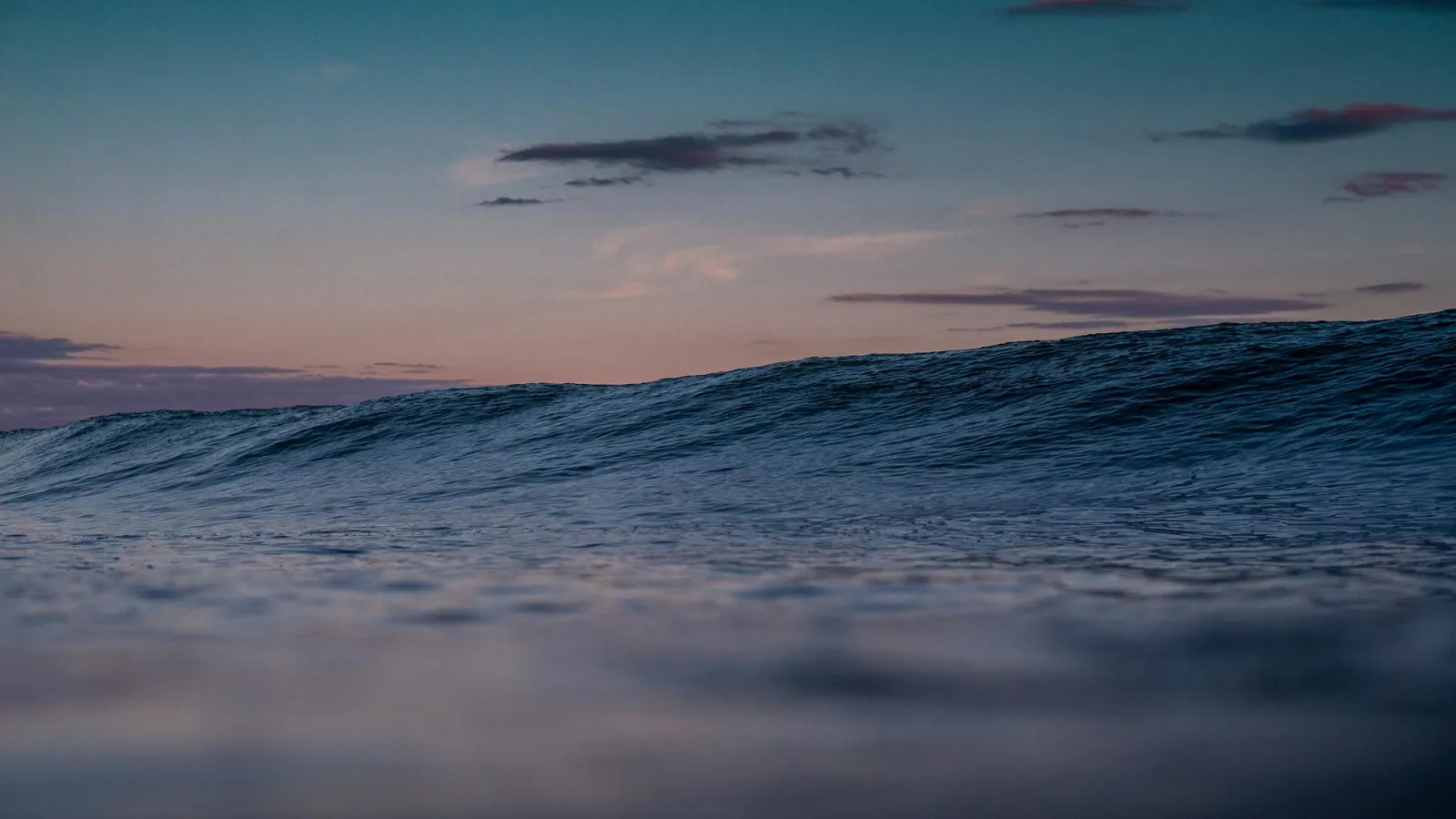 Calm ocean with light waves under blue pink sky.