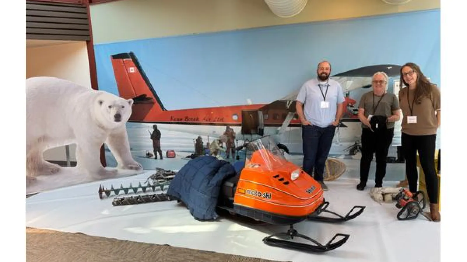 Three people stand smiling in front of a polar fieldwork display.