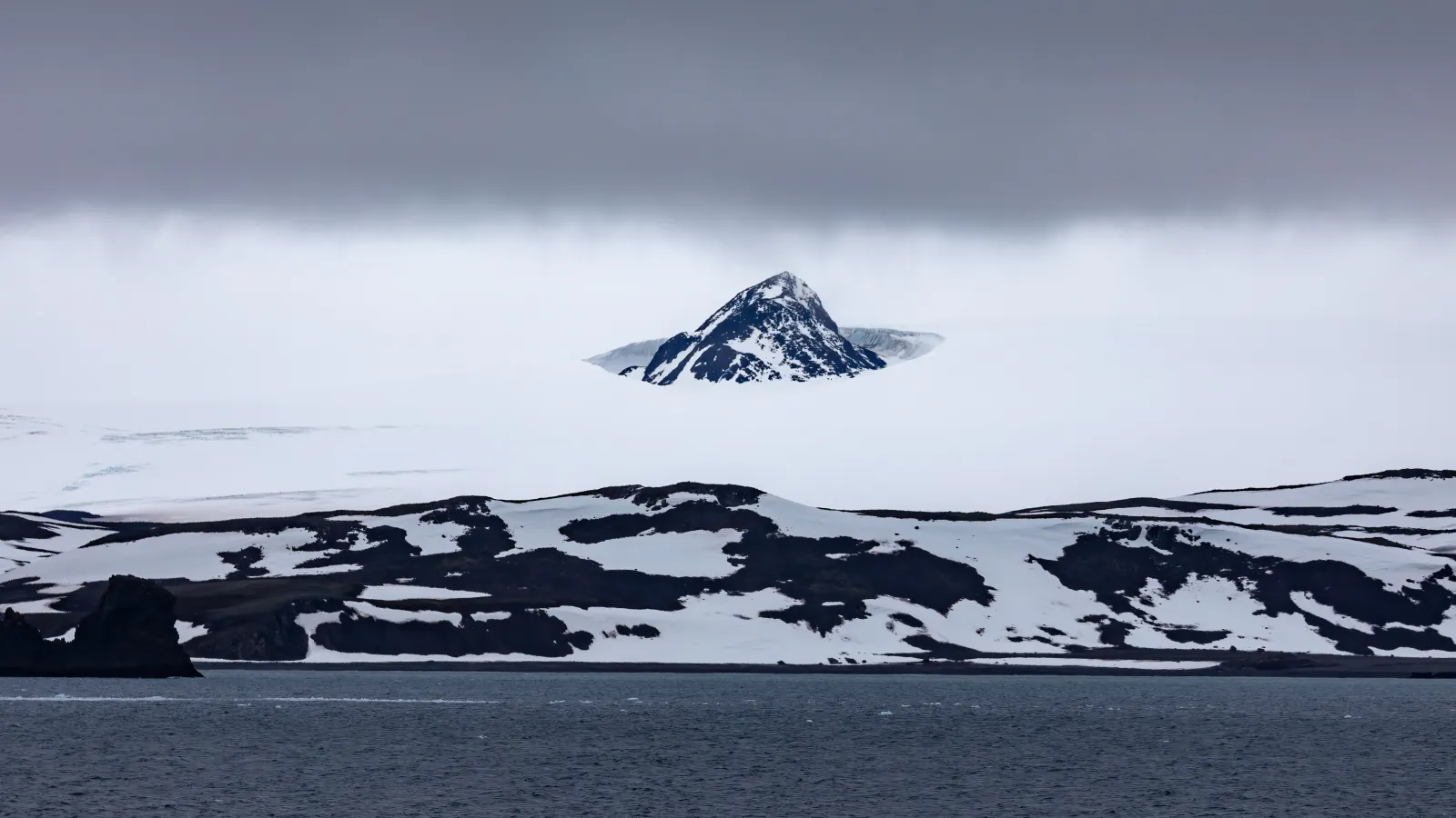 A cold landscape snow covered and an Ocean in the foreground.