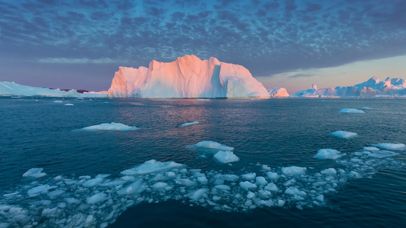 sunlit iceberg with scattered sea ice under a pastel arctic sky