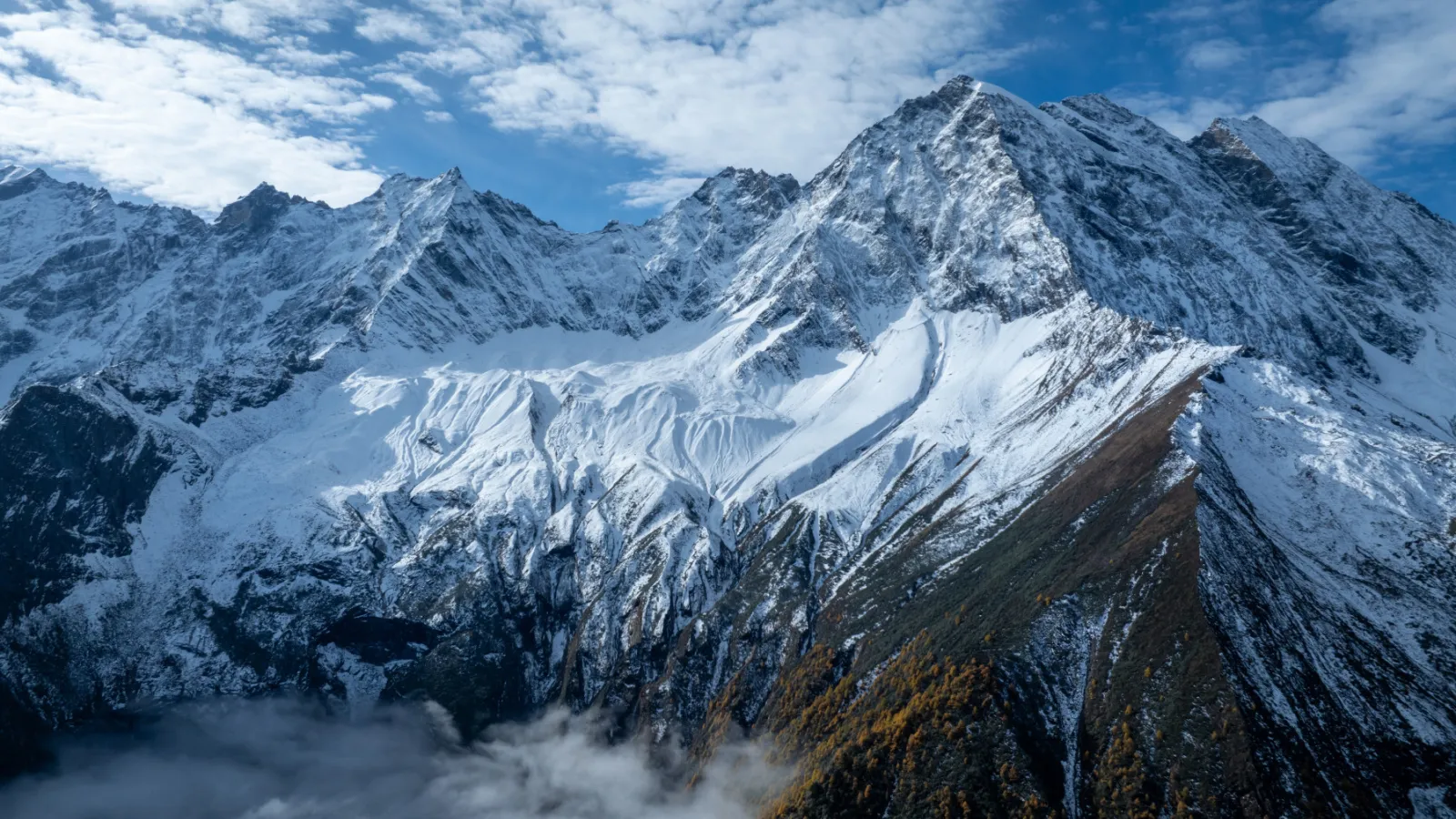Snowy mountain peaks above a cloud-filled valley under a blue sky.