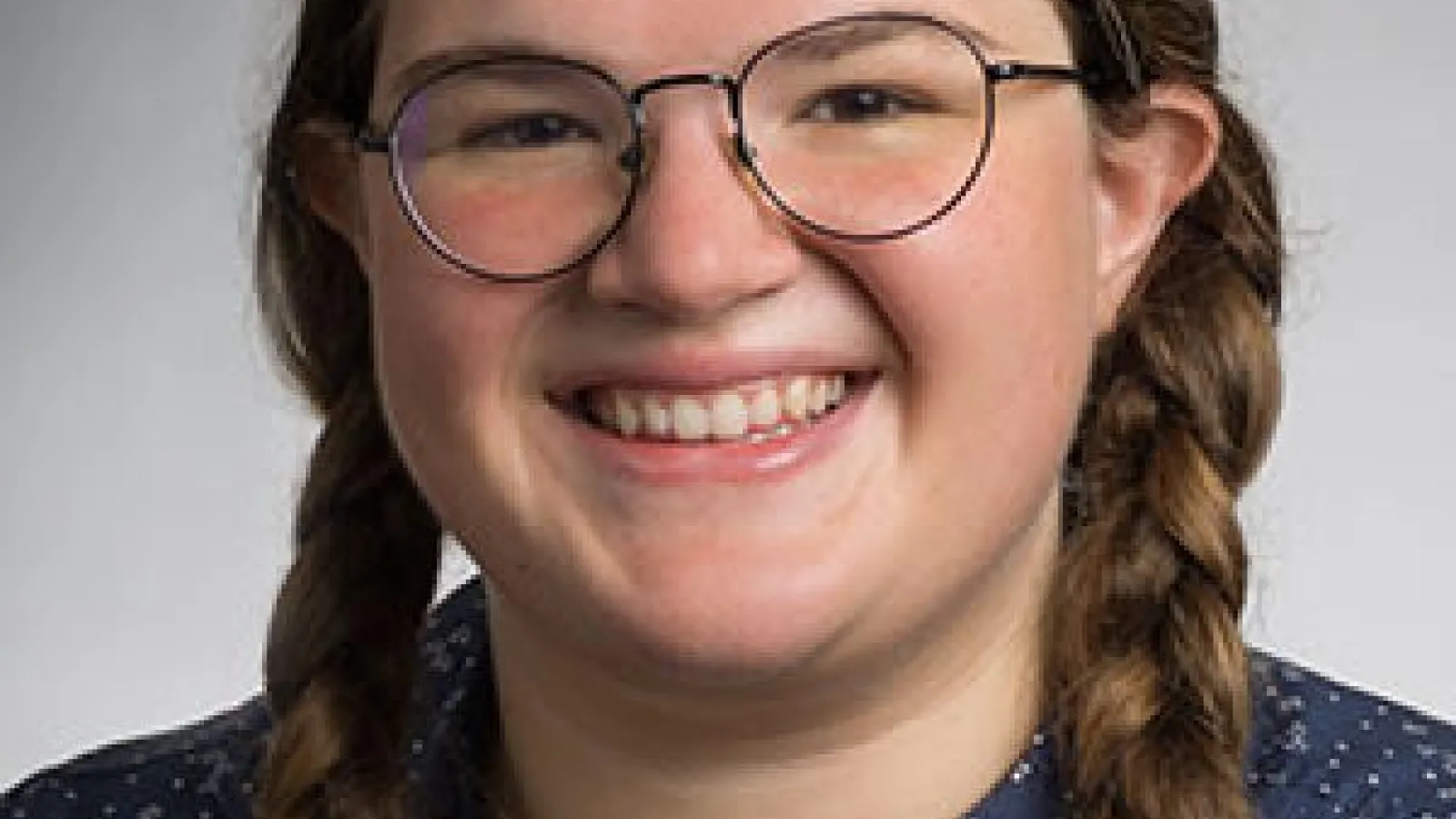 Emily Mazan wearing glasses with braids and a blue shirt smiling. 