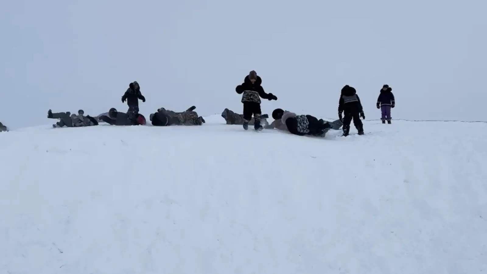 Inuk kids in winter coats stand on top of a snowy hill
