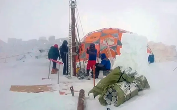 Surrounded by snow, four scientists drill ice cores from the glacier using a tall machine that towers over them