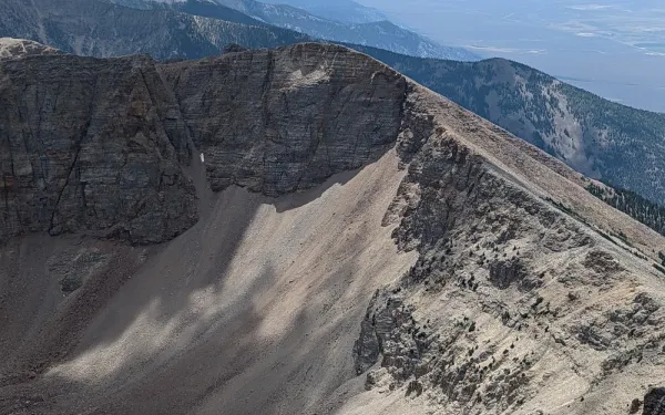Two people walking along the ridge of a  rocky mountain with other mountains in a distance.