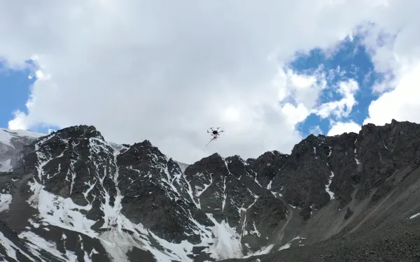 A drone flying over snowy mountain peaks under a partly cloudy sky.