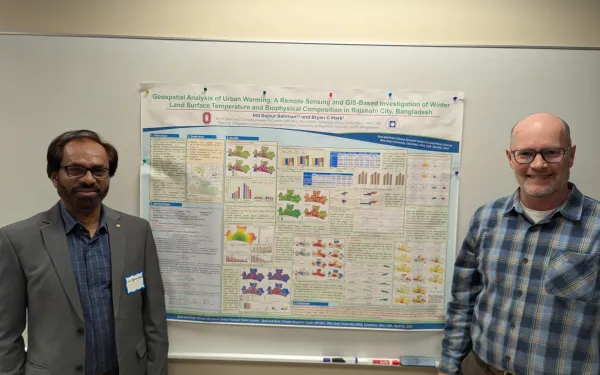 Two people posing with a poster in the middle.
