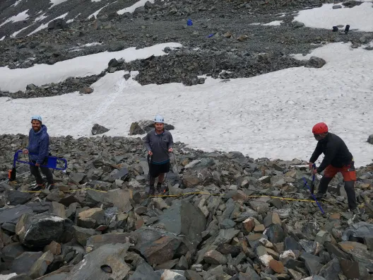 Three people in a snow covered, rocky field working with equipment.