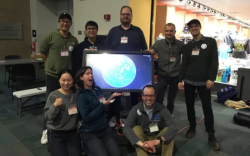 A group of people pose for a photo on front of a screen displaying their work