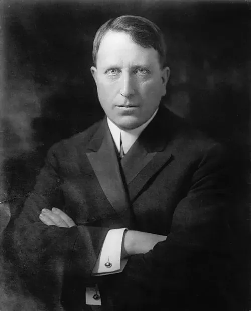 Portrait of a man in a dark suit with folded arms, facing forward.