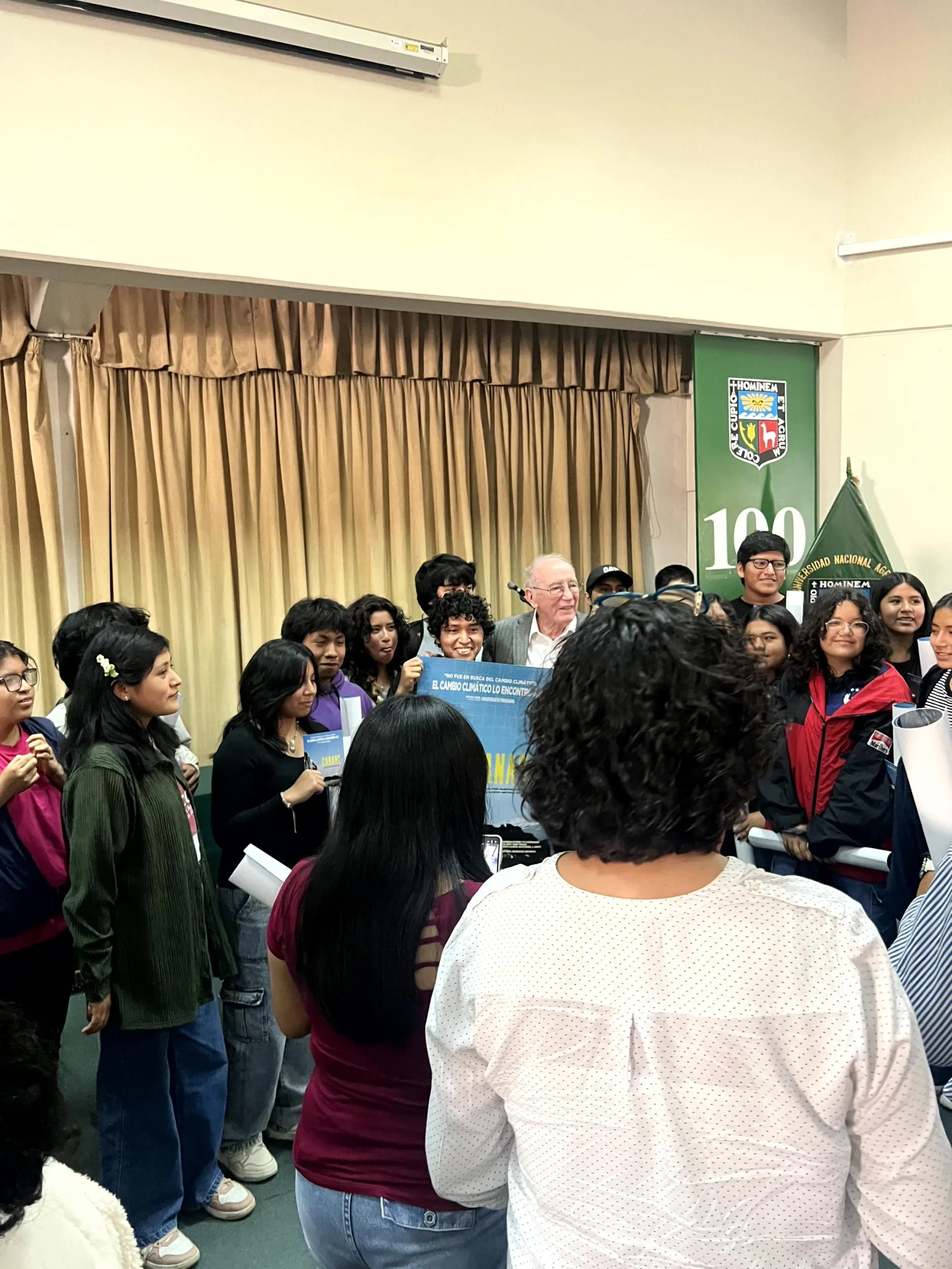 crowd around a person at UNALM event, with a “100” banner in the background.