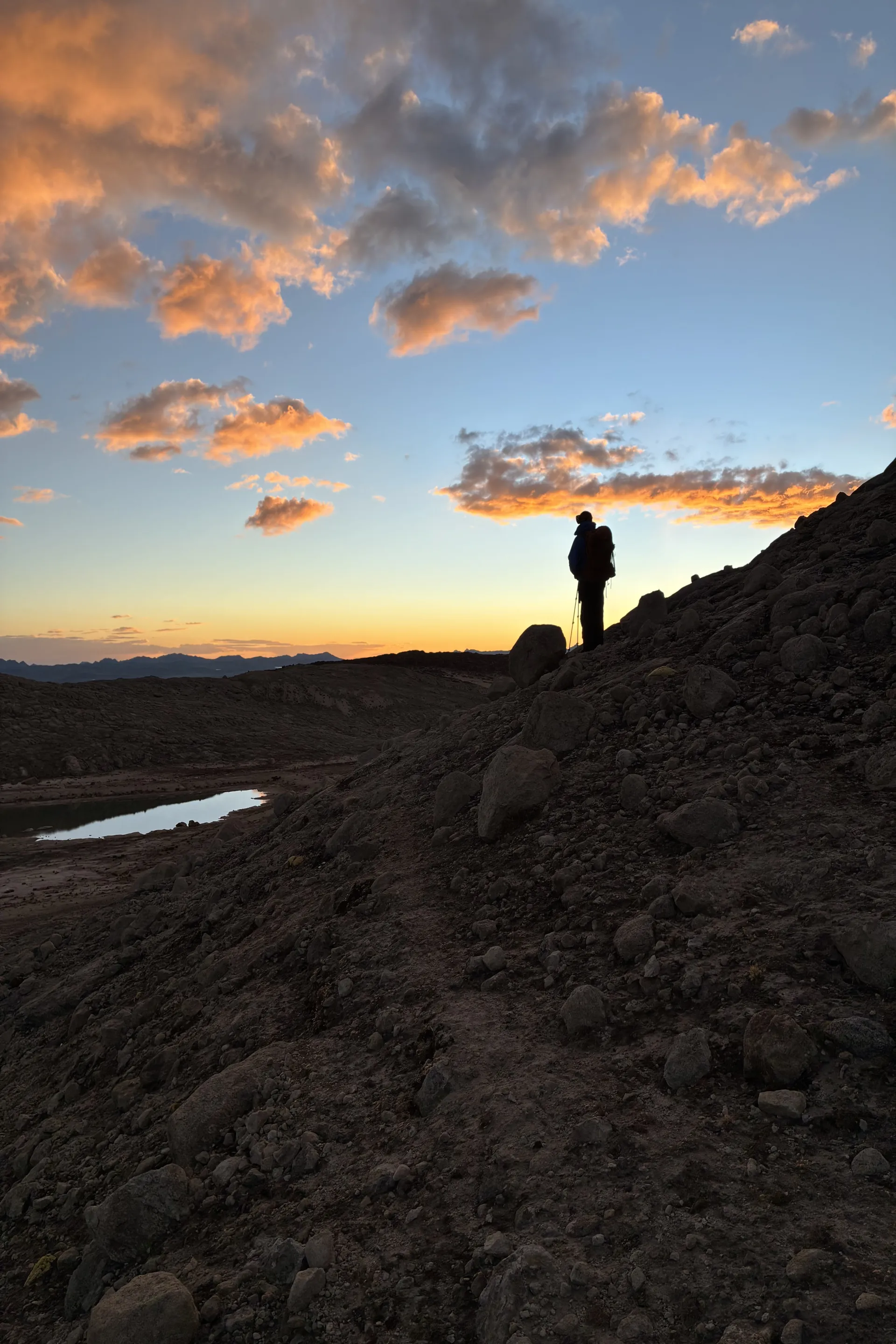 A silhouette stands on the edge of a trail looking out to a pick and yellow sky