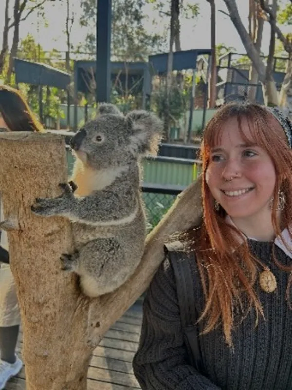A person outdoors standing next to a koala bear