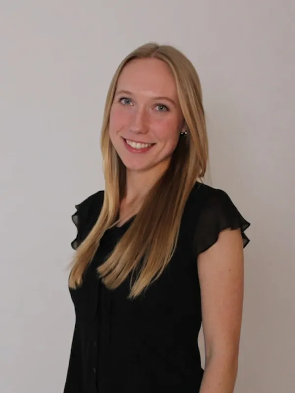 Grace Davis, a woman with blonde hair smiling in a black bouse in front of a grey backdrop.