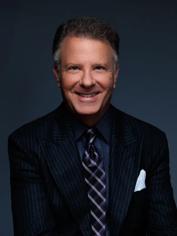 Joseph Manning wearing a suit smiling for the camera in front of a dark blue backdrop.
