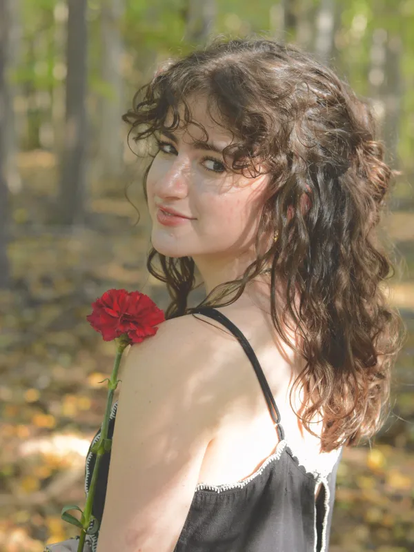 Meredith Button turning towards the camera with a red flower and the forest as a background. 