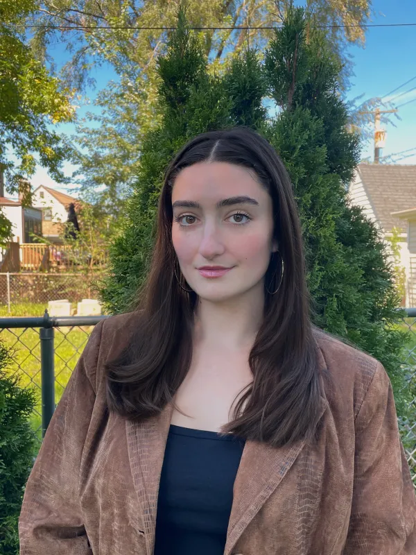 Woman with brown hair poses against a leafy background.