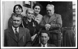 A group of six people, three men and three women. The men are all in suits, the women in dresses with their hair pulled back. The woman in the middle looks much older than the others.