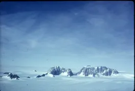 Two rocky mountains peaking through the snow with a great, blue sky with wispy clouds behind them