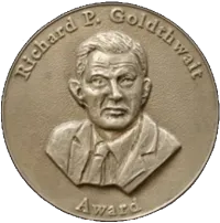 Goldthwait Polar Medal. It is a gold medalion engraved with the head and shoulders of a man with short hair in a suit. On the top and bottom lips of the medalion, the words "Richard P. Goldthwait Award" has been engraved.